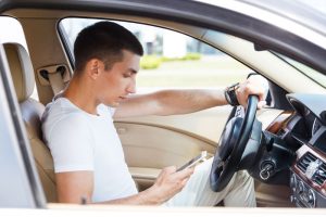 Young man looking at phone texting while driving